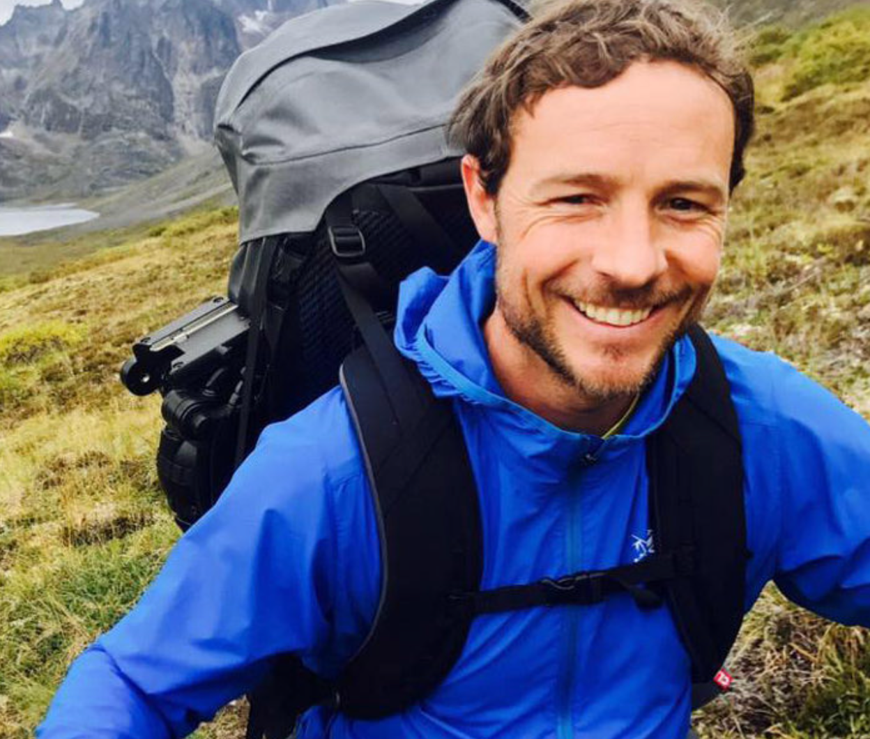 Man smiling while hiking in the mountains with a large backpack.
