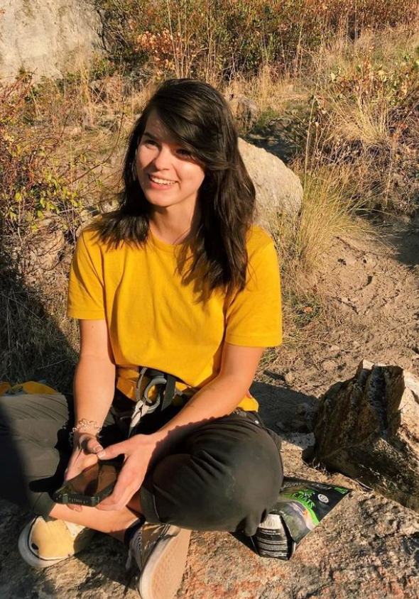 Person in yellow shirt sitting on a rock outdoors, holding a smartphone.